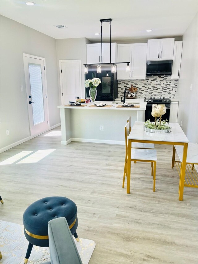 863 Dolly Wright St, Houston, TX 77088 - kitchen with stainless steel microwave, black gas range, light wood-style flooring, tasteful backsplash, and white cabinetry