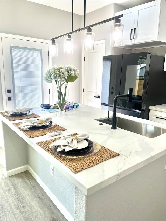 863 Dolly Wright St, Houston, TX 77088 - kitchen with light wood-style floors, white cabinets, an island with sink, light stone countertops, and a sink