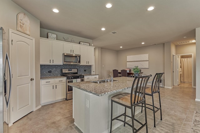 13919 Leigh Lake Ln, Conroe, TX 77384 - kitchen featuring appliances with stainless steel finishes, a kitchen bar, white cabinets, a center island with sink, and light stone counters