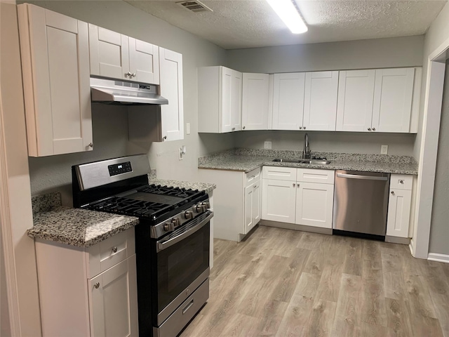 5822 Glenhurst Dr, Houston, TX 77033 - kitchen featuring stainless steel appliances, under cabinet range hood, a textured ceiling, light wood-type flooring, and light stone countertops