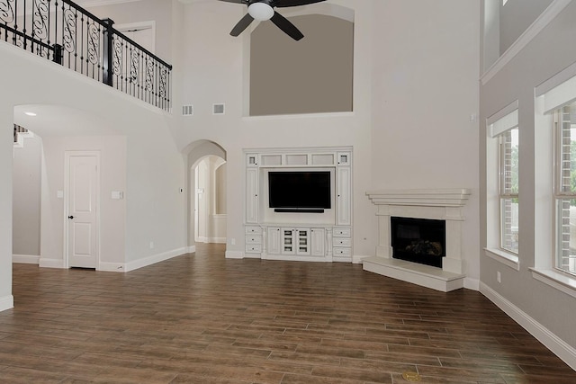 31338 Shadow Branch Ln, Spring, TX 77386 - unfurnished living room featuring a ceiling fan, a towering ceiling, arched walkways, plenty of natural light, and wood finished floors