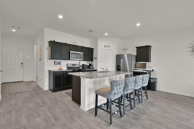 14212 Dream Rd, New Caney, TX 77357 - kitchen with appliances with stainless steel finishes, a kitchen island with sink, a kitchen breakfast bar, a sink, and light stone counters