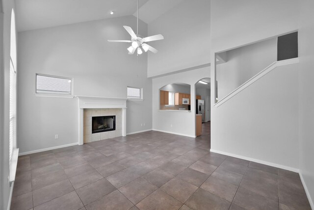 25819 Oakridge Forest Ln, Spring, TX 77386 - unfurnished living room featuring ceiling fan, high vaulted ceiling, arched walkways, a tile fireplace, and baseboards