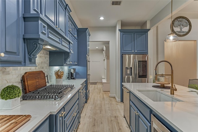 11 Hillsborough Dr E, Montgomery, TX 77356 - kitchen with blue cabinets, a sink, stainless steel appliances, light wood-style floors, and tasteful backsplash