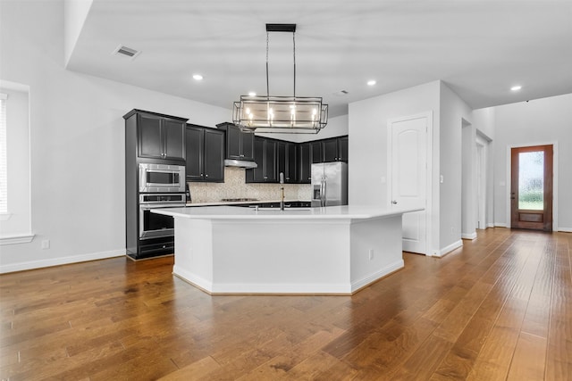 148 Gray Pine Grove Way, Conroe, TX 77318 - kitchen featuring appliances with stainless steel finishes, dark cabinetry, light countertops, backsplash, and a kitchen island with sink