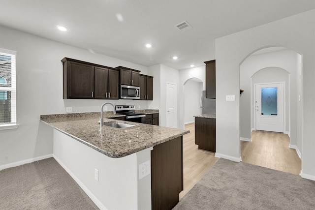 22807 Gentle Shadow Dr, Hockley, TX 77447 - kitchen featuring appliances with stainless steel finishes, a sink, arched walkways, dark brown cabinetry, and light stone counters