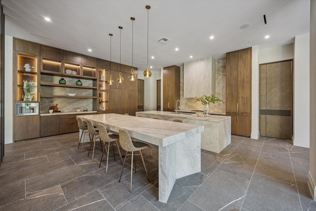 9010 Memorial Dr, Houston, TX 77024 - kitchen with a spacious island, modern cabinets, brown cabinets, a sink, and recessed lighting
