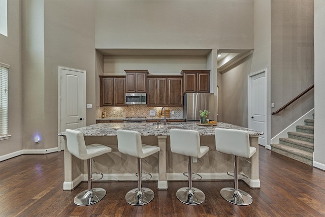 114 Cedar Brush Ct, Montgomery, TX 77316 - kitchen with stainless steel appliances, a high ceiling, a kitchen island with sink, a breakfast bar, and dark wood finished floors
