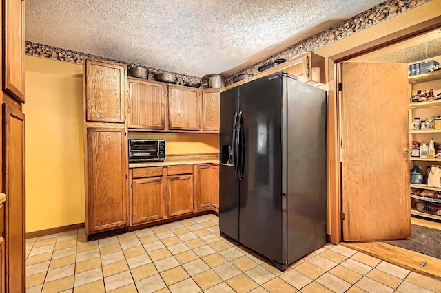 170 Trails End Dr, Cleveland, TX 77328 - kitchen featuring black fridge, a textured ceiling, brown cabinetry, light countertops, and light tile patterned flooring