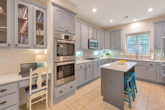 126 S Bluff Creek Cir, The Woodlands, TX 77382 - kitchen featuring gray cabinetry, stainless steel appliances, a kitchen breakfast bar, decorative backsplash, and a center island