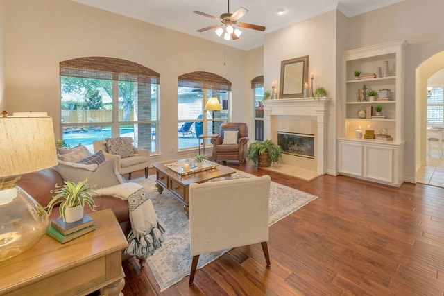 126 S Bluff Creek Cir, The Woodlands, TX 77382 - living room with arched walkways, ceiling fan, a glass covered fireplace, wood finished floors, and crown molding