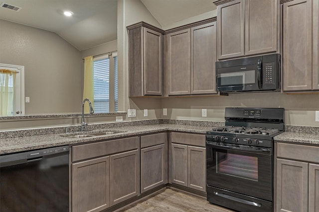 14208 Sedona Ridge Dr, Conroe, TX 77303 - kitchen with black appliances, lofted ceiling, light wood-type flooring, and light stone counters