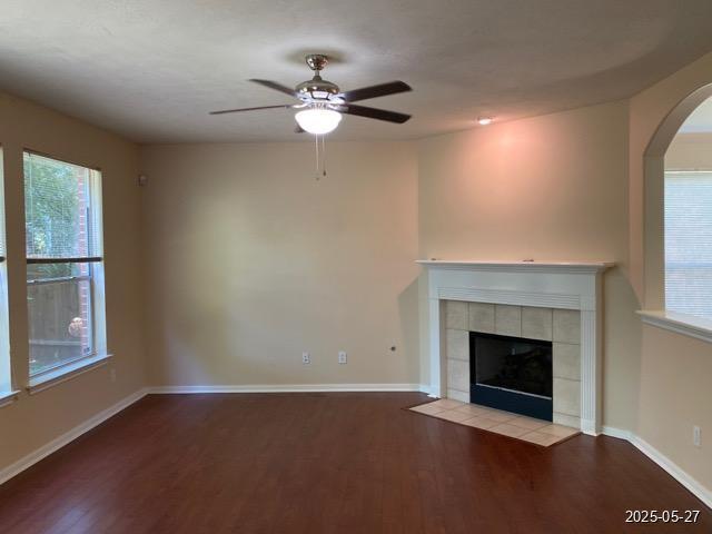 151 Prairie Dawn Cir, Conroe, TX 77385 - unfurnished living room with wood finished floors, ceiling fan, a tiled fireplace, baseboards, and arched walkways