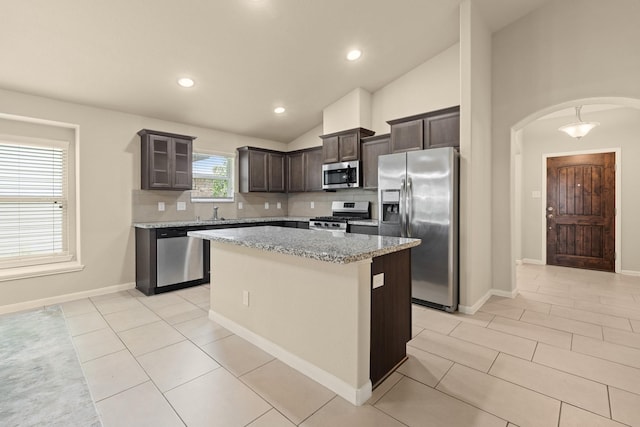19110 Macallan Ln, Katy, TX 77449 - kitchen featuring appliances with stainless steel finishes, arched walkways, a center island, dark brown cabinets, and backsplash