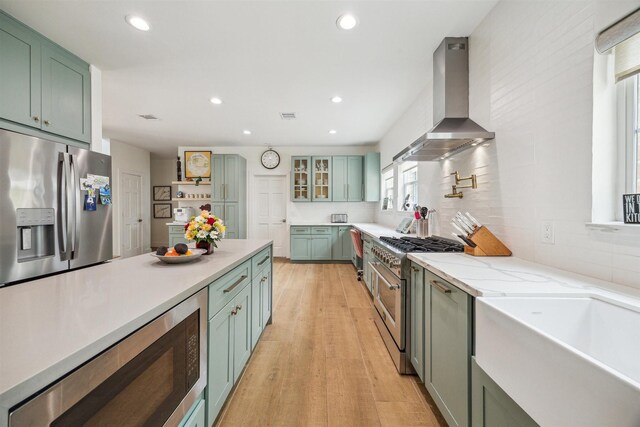 1215 Heathwood Dr, Houston, TX 77077 - kitchen featuring wall chimney exhaust hood, stainless steel appliances, green cabinetry, light wood-style flooring, and recessed lighting