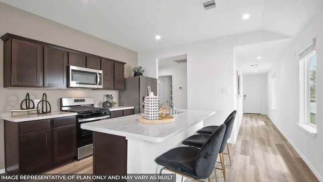 5446 Pinetree Crescent Ln, Spring, TX 77373 - kitchen featuring appliances with stainless steel finishes, light countertops, a kitchen island with sink, dark brown cabinetry, and light wood-type flooring