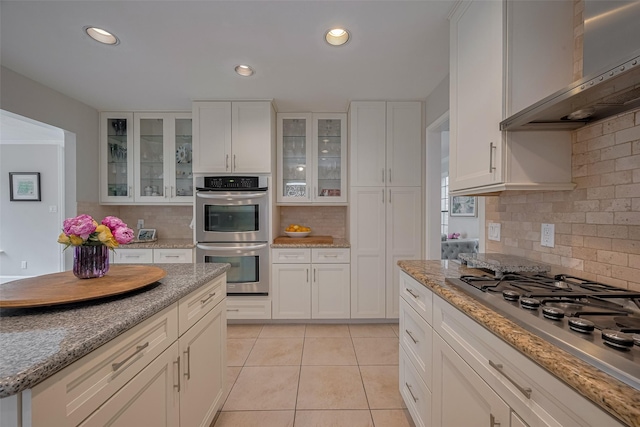 12214 Clearfork Dr, Houston, TX 77077 - kitchen featuring appliances with stainless steel finishes, wall chimney exhaust hood, decorative backsplash, light tile patterned flooring, and white cabinets