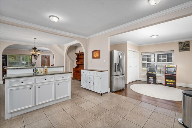 1906 Pasadena St, Houston, TX 77023 - kitchen with stainless steel refrigerator with ice dispenser, light tile patterned flooring, ornamental molding, white cabinetry, and arched walkways