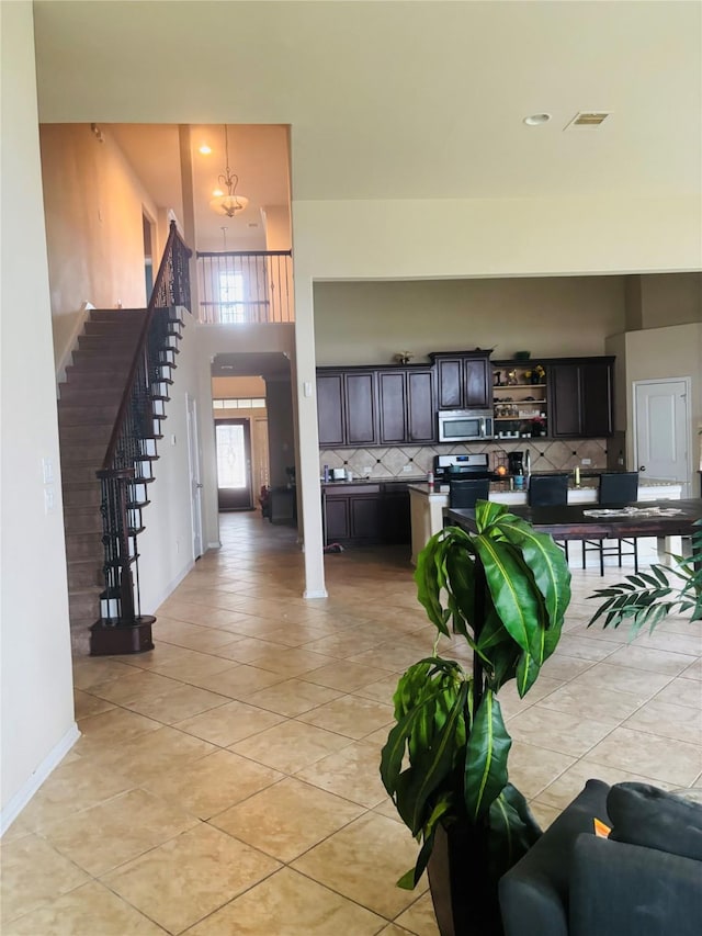 9615 Emerald Briar Ln, Rosenberg, TX 77469 - kitchen featuring stainless steel microwave, tasteful backsplash, light tile patterned floors, open shelves, and a towering ceiling