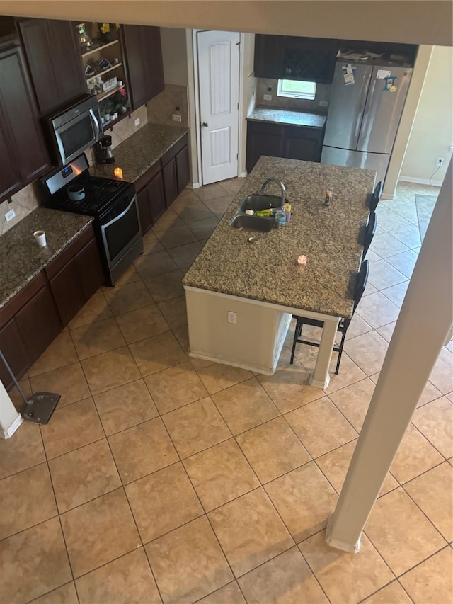 9615 Emerald Briar Ln, Rosenberg, TX 77469 - kitchen featuring appliances with stainless steel finishes, light tile patterned floors, a center island with sink, dark stone counters, and decorative backsplash