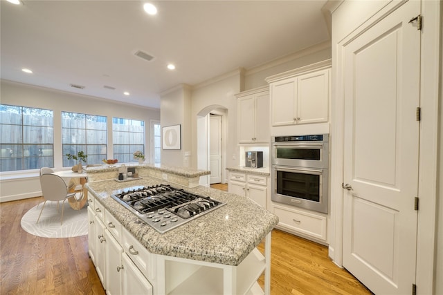 4035 Gramercy St, Houston, TX 77025 - kitchen with stainless steel appliances, a center island, arched walkways, light stone countertops, and light wood-type flooring