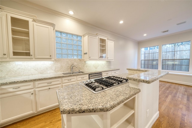 4035 Gramercy St, Houston, TX 77025 - kitchen featuring stainless steel appliances, a center island, light wood-type flooring, decorative backsplash, and ornamental molding