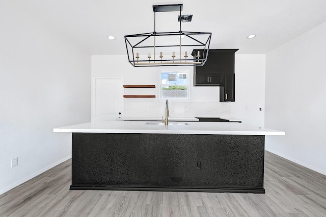 7939 Goode St, Houston, TX 77012 - kitchen with a center island with sink, light countertops, a chandelier, light wood-style floors, and dark cabinets