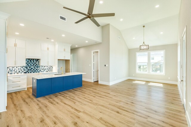 591 Pompano Dr, Freeport, TX 77541 - kitchen featuring white cabinets, backsplash, light wood-style floors, a center island with sink, and high vaulted ceiling