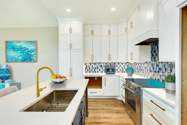 591 Pompano Dr, Freeport, TX 77541 - kitchen with stainless steel range with electric cooktop, custom exhaust hood, white cabinets, light countertops, and tasteful backsplash