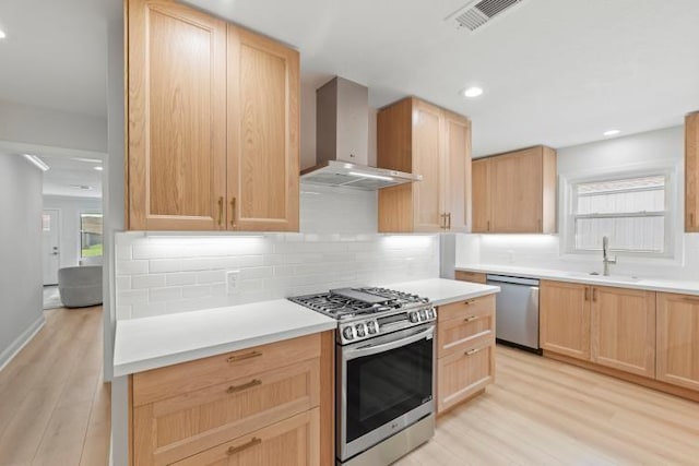 4406 Merwin St, Houston, TX 77027 - kitchen featuring appliances with stainless steel finishes, wall chimney exhaust hood, light brown cabinets, light wood-style flooring, and recessed lighting