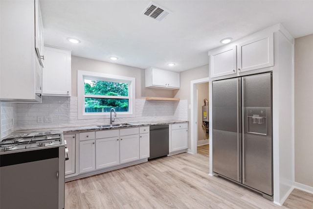 5858 Beldart St, Houston, TX 77033 - kitchen with appliances with stainless steel finishes, white cabinetry, light wood-style flooring, light stone countertops, and decorative backsplash