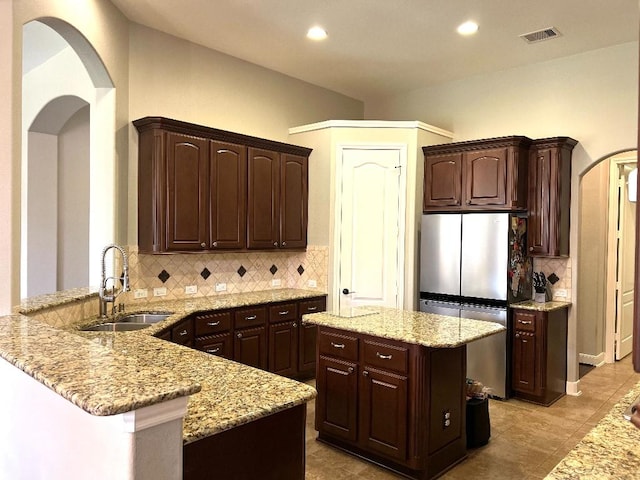 13839 Oak Fair Bnd, Cypress, TX 77429 - kitchen featuring freestanding refrigerator, arched walkways, a peninsula, tasteful backsplash, and light stone counters