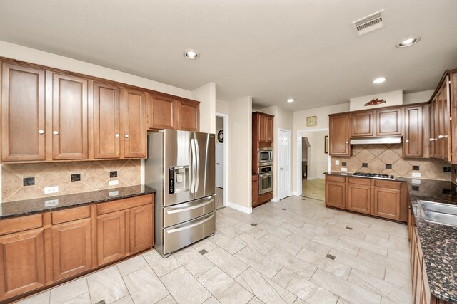 20718 Mansfield Bay Ln, Richmond, TX 77407 - kitchen with stainless steel appliances, under cabinet range hood, brown cabinetry, dark stone countertops, and recessed lighting