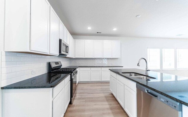 25035 Apricot Ct, Montgomery, TX 77316 - kitchen featuring appliances with stainless steel finishes, light wood-type flooring, backsplash, white cabinetry, and dark stone counters