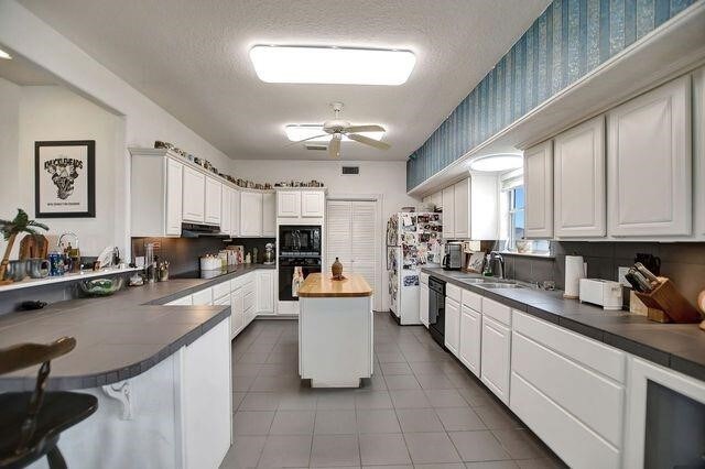 23002 Lunes St, Galveston, TX 77554 - kitchen featuring black appliances, tile patterned flooring, a ceiling fan, butcher block counters, and wallpapered walls