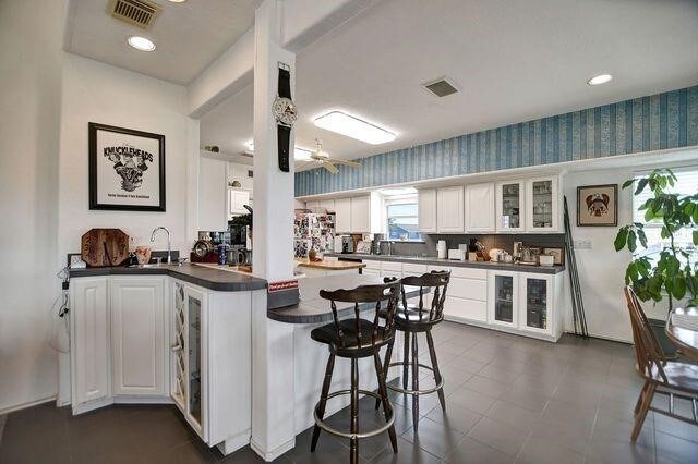 23002 Lunes St, Galveston, TX 77554 - kitchen with dark countertops, a peninsula, glass insert cabinets, white cabinetry, and wallpapered walls