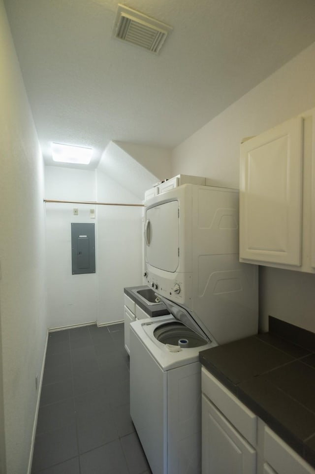 23002 Lunes St, Galveston, TX 77554 - laundry room with stacked washer and clothes dryer, cabinet space, electric panel, and dark tile patterned floors