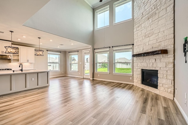 2008 Bristol Cliff Ln, Pearland, TX 77089 - unfurnished living room with plenty of natural light, light wood-style flooring, ornamental molding, a stone fireplace, and a towering ceiling