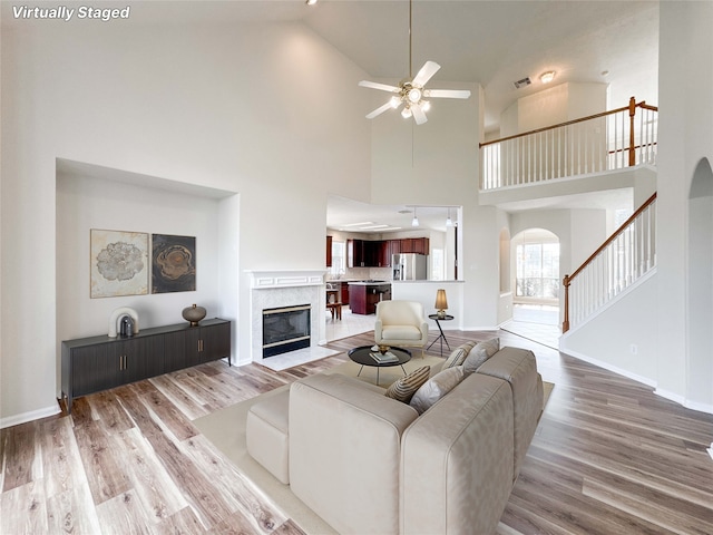 3106 Alexandros Ct, Pearland, TX 77584 - living room featuring arched walkways, a ceiling fan, light wood-style flooring, high vaulted ceiling, and a high end fireplace