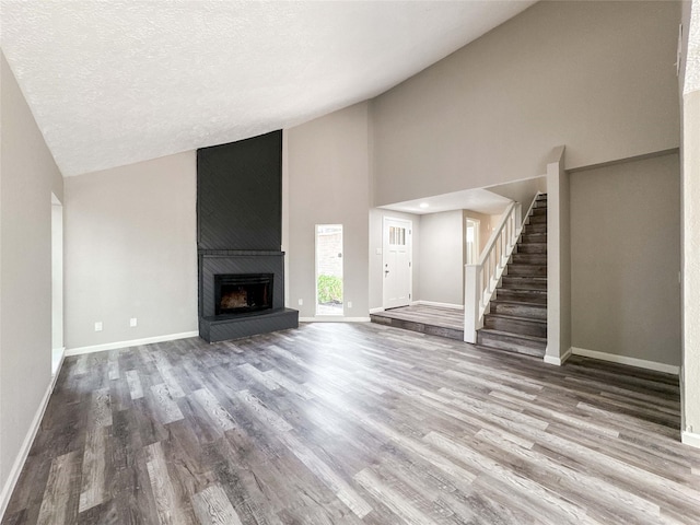 10610 Mills Prairie St, Houston, TX 77070 - unfurnished living room featuring wood finished floors, high vaulted ceiling, stairs, a fireplace, and a textured ceiling