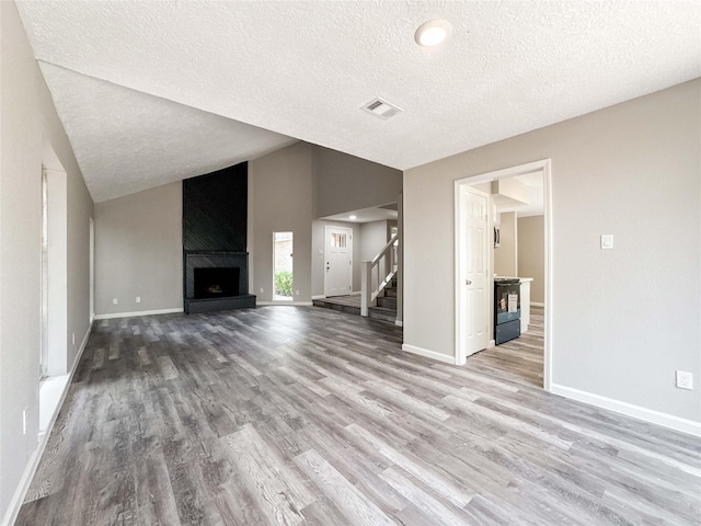 10610 Mills Prairie St, Houston, TX 77070 - unfurnished living room with a large fireplace, wood finished floors, a textured ceiling, stairs, and vaulted ceiling