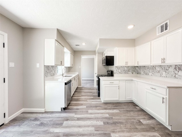 10610 Mills Prairie St, Houston, TX 77070 - kitchen featuring appliances with stainless steel finishes, decorative backsplash, white cabinets, light wood-style floors, and recessed lighting
