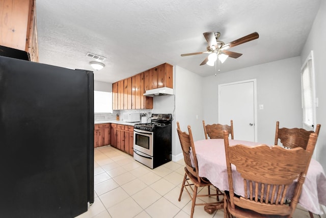 2811 Wentworth Ln, Pasadena, TX 77506 - kitchen featuring stainless steel gas stove, freestanding refrigerator, a ceiling fan, under cabinet range hood, and brown cabinets