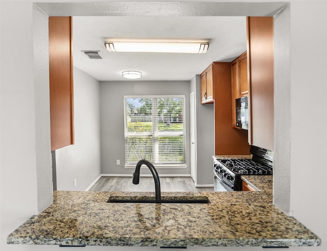 3445 Van Ness Dr, Alvin, TX 77511 - kitchen featuring gas range, light wood-style flooring, brown cabinets, stone countertops, and black microwave