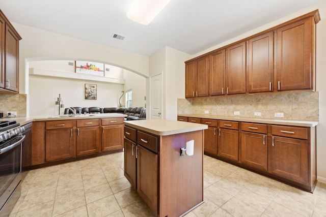 11134 Sun River Falls Dr, Humble, TX 77396 - kitchen with arched walkways, stainless steel range with gas stovetop, a peninsula, light countertops, and tasteful backsplash