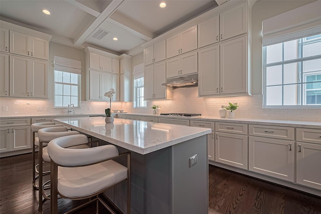 817 Blackshire Ln, Houston, TX 77055 - kitchen featuring under cabinet range hood, dark wood-type flooring, a kitchen island, decorative backsplash, and beam ceiling