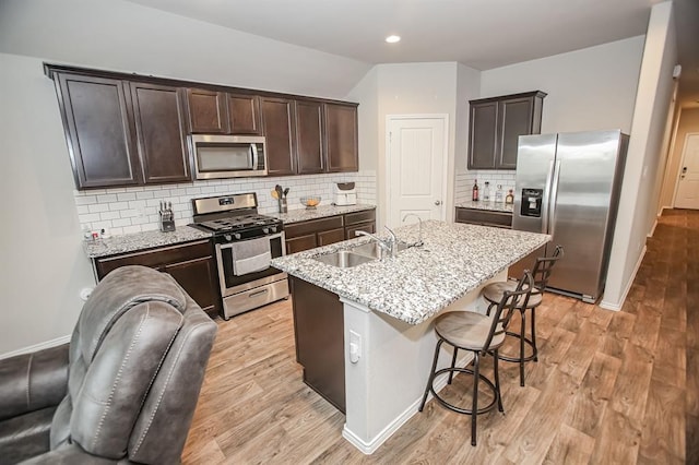 919 Bright Lotus Ln, Rosharon, TX 77583 - kitchen featuring appliances with stainless steel finishes, dark brown cabinets, light stone counters, a kitchen bar, and tasteful backsplash