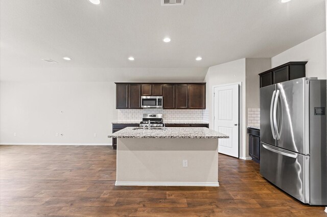 919 Bright Lotus Ln, Rosharon, TX 77583 - kitchen featuring appliances with stainless steel finishes, backsplash, a kitchen island with sink, dark wood-style flooring, and recessed lighting