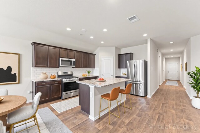 919 Bright Lotus Ln, Rosharon, TX 77583 - kitchen with appliances with stainless steel finishes, dark brown cabinets, decorative backsplash, a center island, and recessed lighting