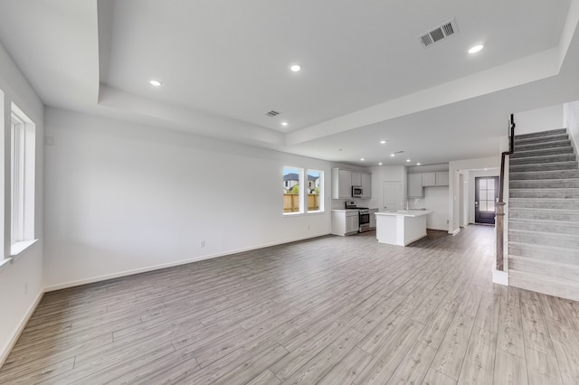 1235 Buffalo Run, Tomball, TX 77375 - unfurnished living room featuring stairway, light wood-style floors, a raised ceiling, and recessed lighting